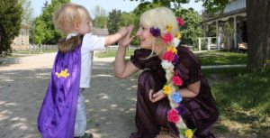 A lady in costume high-fiving a little girl in a cape.