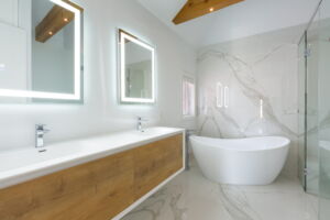 Spa-inspired primary bathroom with marble-look tile, illuminated mirrors and exposed timber ceiling beams in this Etobicoke residence at 28 Martin Grove Road